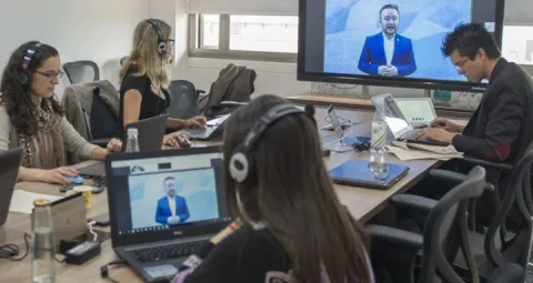 Personas atentas a una reunión, algunos tomando notas o escribiendo en sus portátiles.