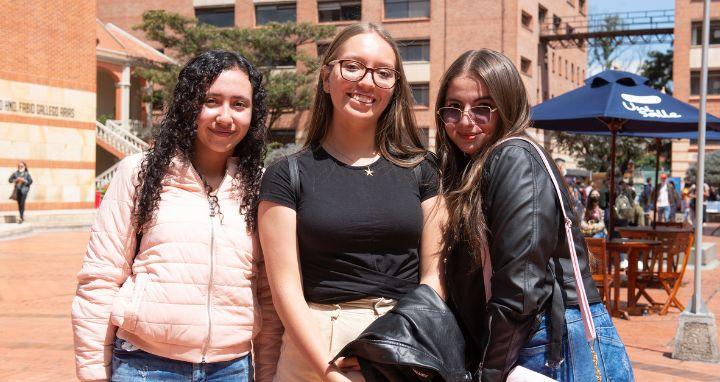 Tres jovenes mujeres de pie al aire libre en un patio con edificios de ladrillo...